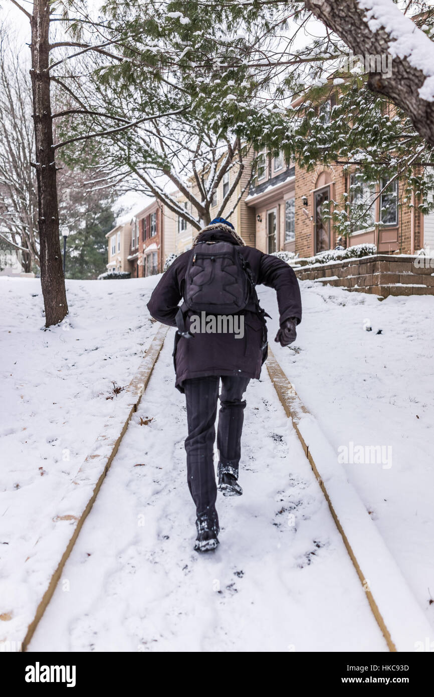 Homme qui court sur le trottoir couvert de neige de l'hiver sur la pente de la colline dans le quartier Banque D'Images