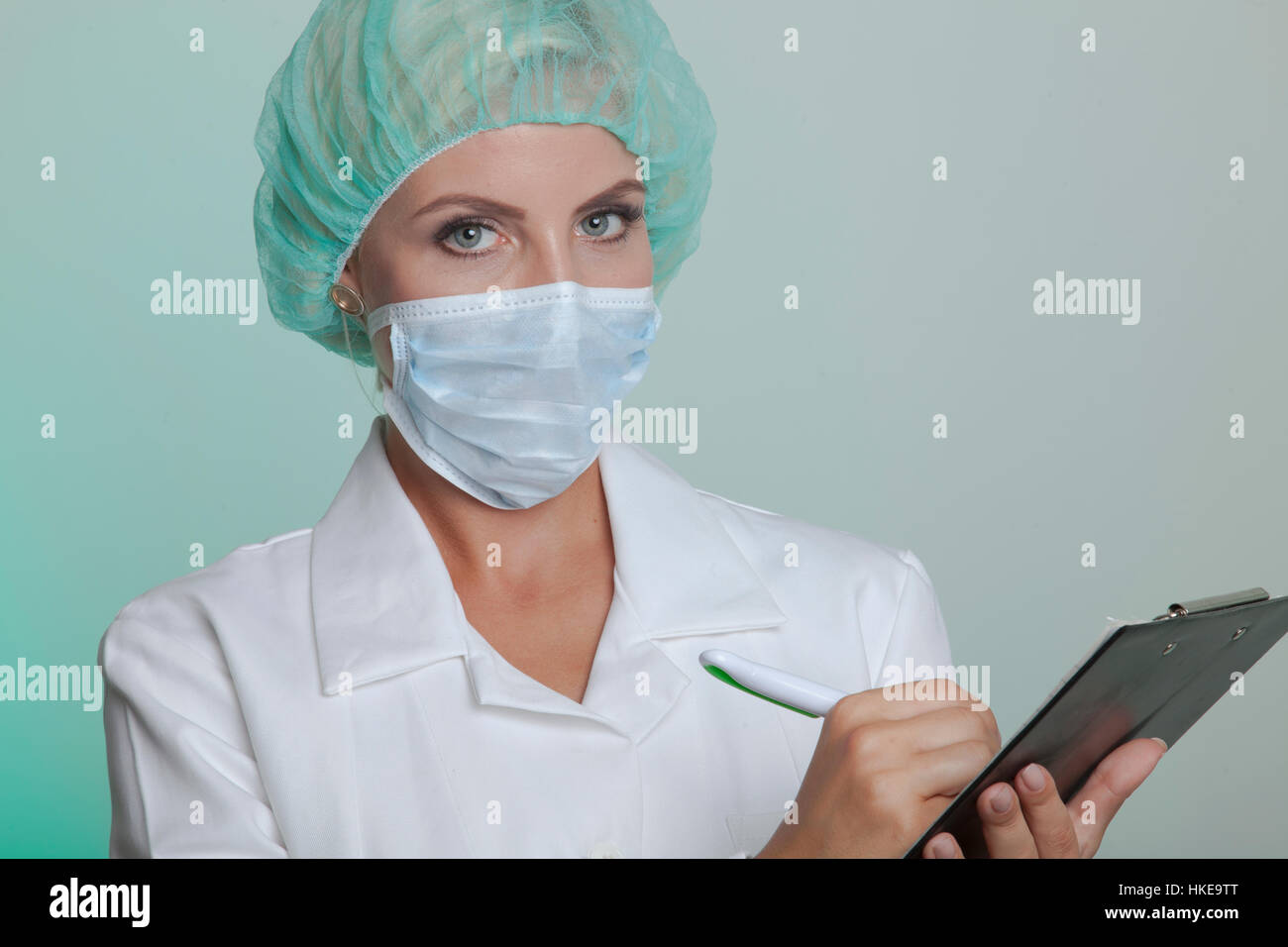 Femme médecin dans un manteau blanc portant bonnet de cheveux et protège-dents a un stéthoscope autour de son cou tandis que l'écriture de certains renseignements importants à ses cl Banque D'Images