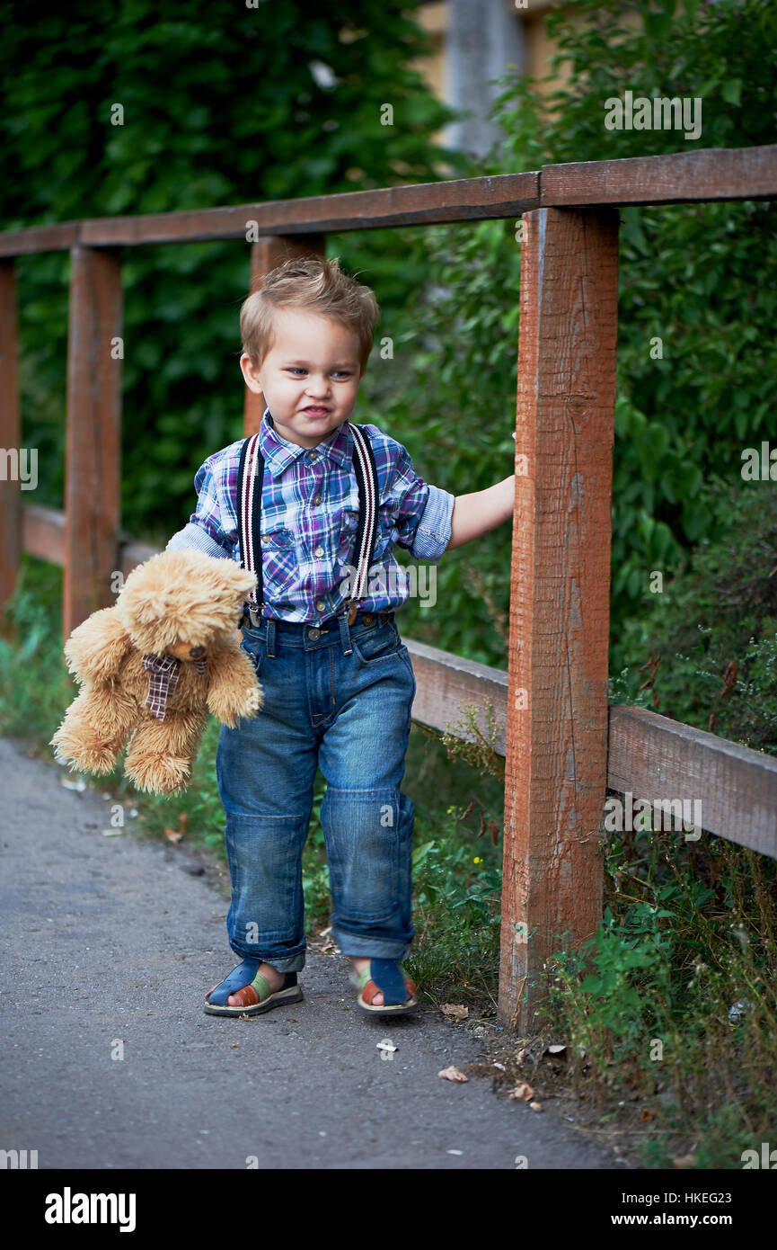 Adorable petit garçon debout près d'un élégant en bois brun , avec bretelles  jeans et chemise à carreaux . Les souvenirs de l'enfance insouciante Photo  Stock - Alamy