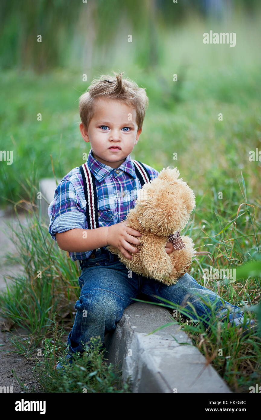 Mignon petit garçon assis et serrant son ours en peluche, jeans élégant  avec bretelles chemise à carreaux . Les souvenirs de l'enfance insouciante  Photo Stock - Alamy