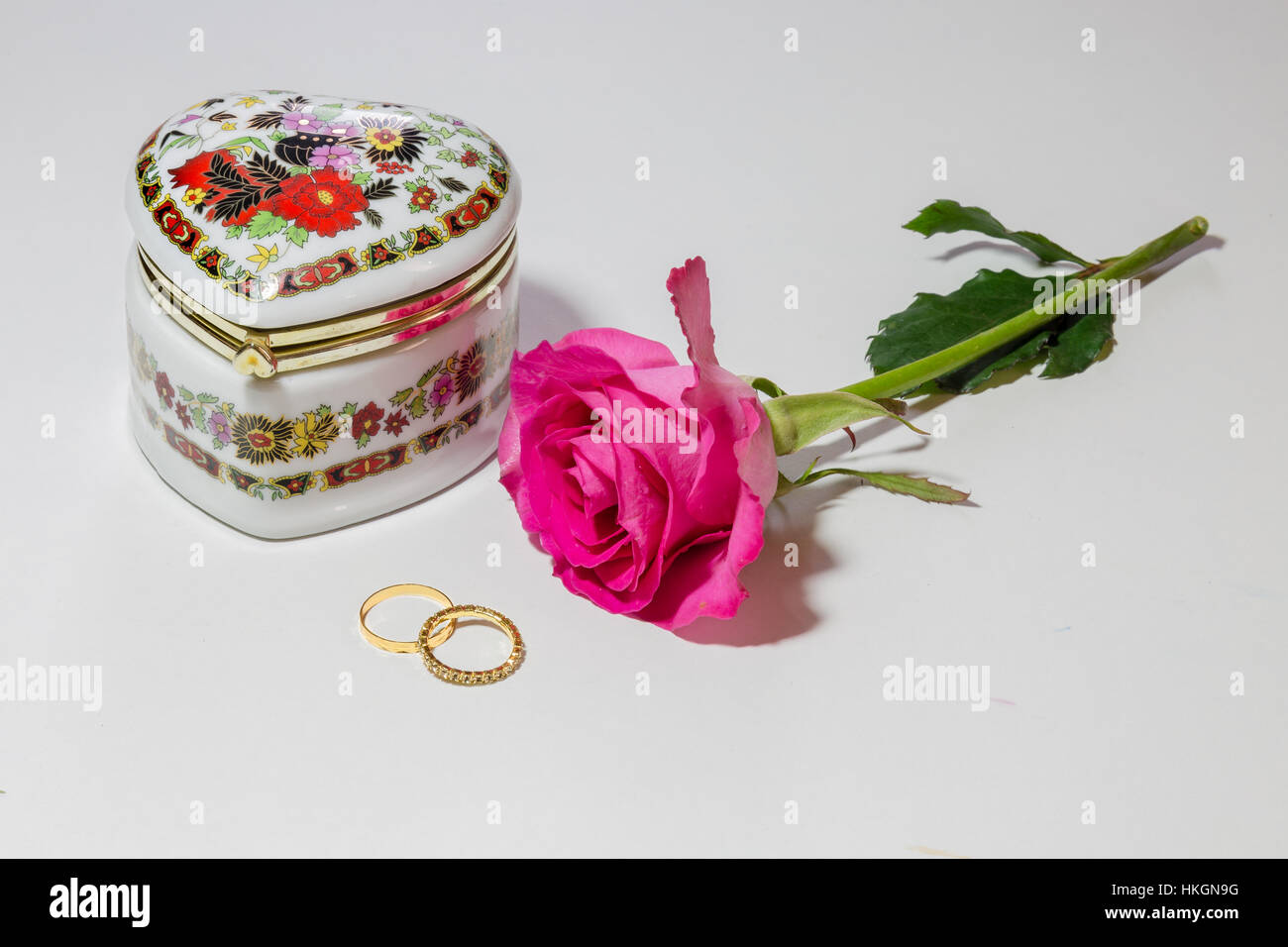 Saint Valentin romantique décorée avec du contenu dans un boîtier cristal avec une rose rose et or bagues en fond blanc. Banque D'Images