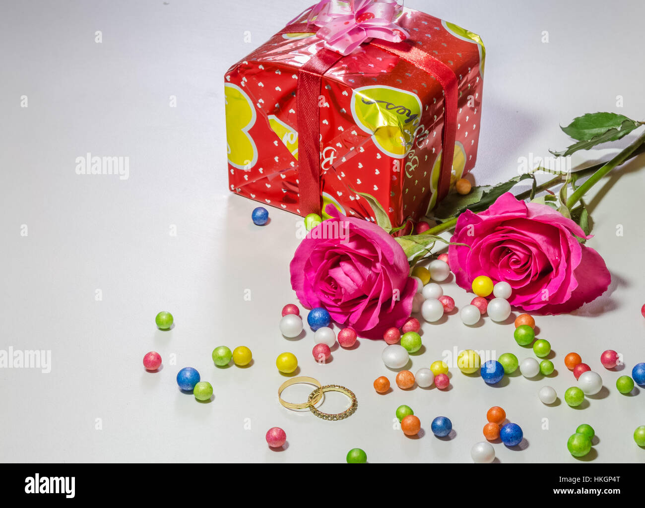 Roses rose vif avec élément de cadeau enveloppé et les alliances avec des boules de papier multicolore isolé en fond blanc. Banque D'Images