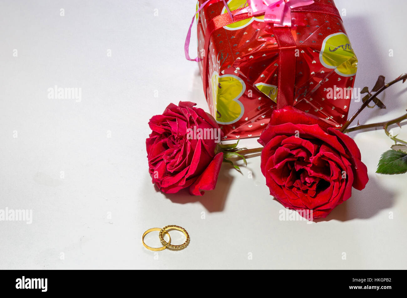 Roses rouge vif avec de l'or et des bagues de fiançailles cadeau enveloppé isolé en blanc. L'espace blanc pour le contenu du message romantique. Banque D'Images