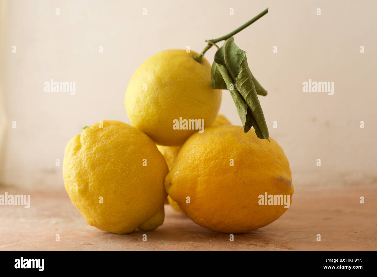 Une pile de quatre citrons avec un peu de feuillage contre un fond rustique Banque D'Images
