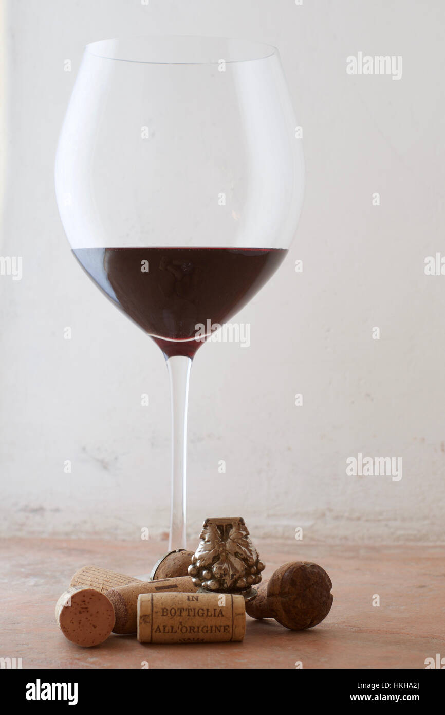 Un grand verre de vin rouge avec un arrangement de bouchons et d'un bouchon de bouteille d'argent à la base Banque D'Images