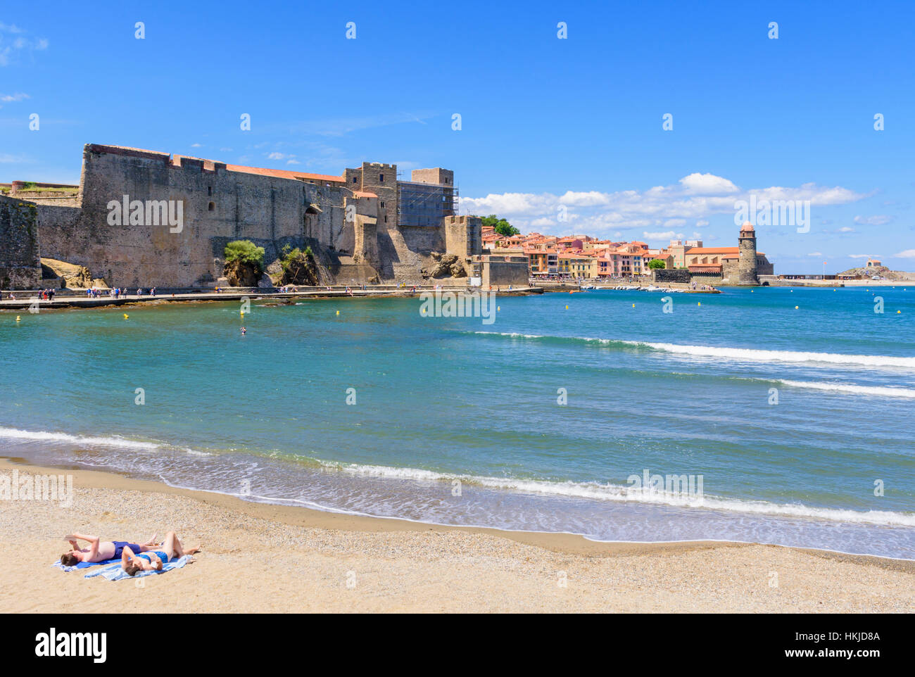 Couple de bronzer sur une plage de port d'Avall dominé par le Château Royal de Collioure et l'église de Notre-Dame des Anges, Collioure, France Banque D'Images