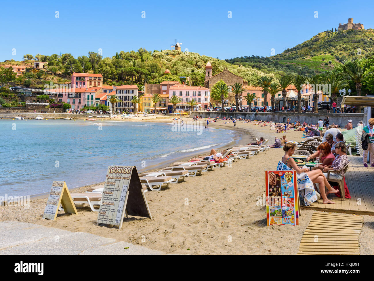 Les gens à un café sur la plage Plage de port d'Avall dominé par le Fort St Elme et le moulin, Collioure, Côte Vermeille, France Banque D'Images
