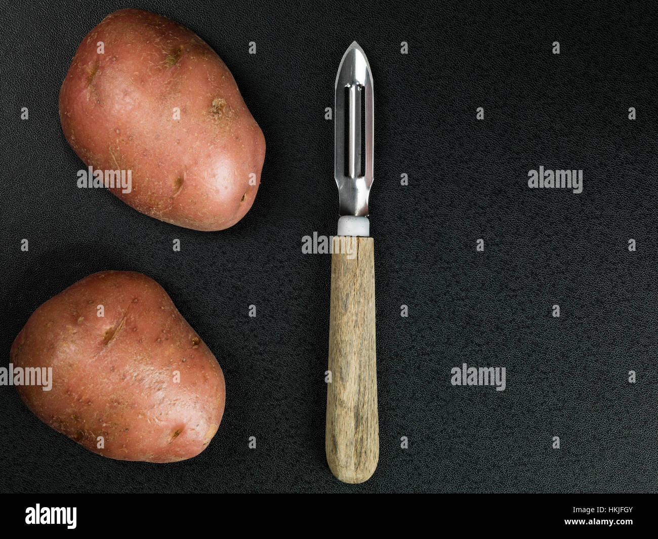 Éplucheuse de pommes de terre traditionnelles avec deux pommes de terre non cuites Banque D'Images