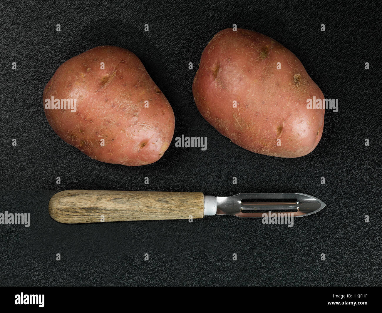 Éplucheuse de pommes de terre traditionnelles avec deux pommes de terre non cuites Banque D'Images