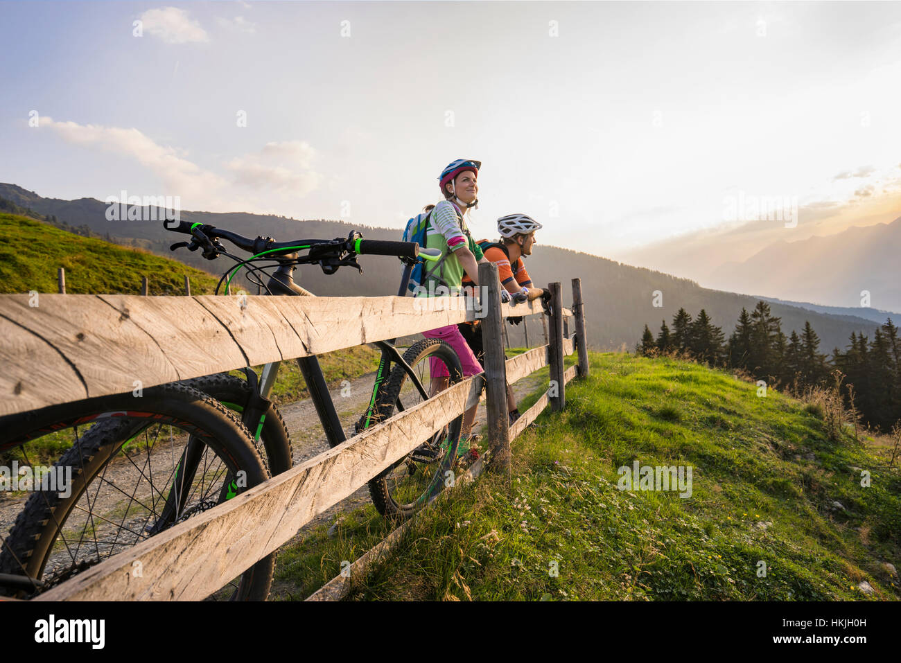 Jeune couple de vététistes par permanent à la clôture de bois à voir pendant le coucher du soleil, Zillertal, Tyrol, Autriche Banque D'Images