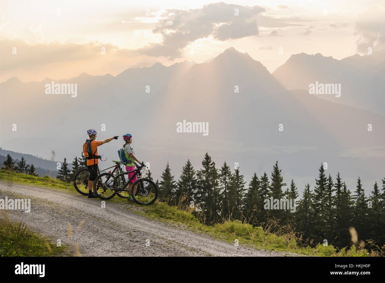 Jeune couple de cyclistes de montagne debout sur chemin de terre et à la recherche à vue pendant le coucher du soleil, Zillertal, Tyrol, Autriche Banque D'Images