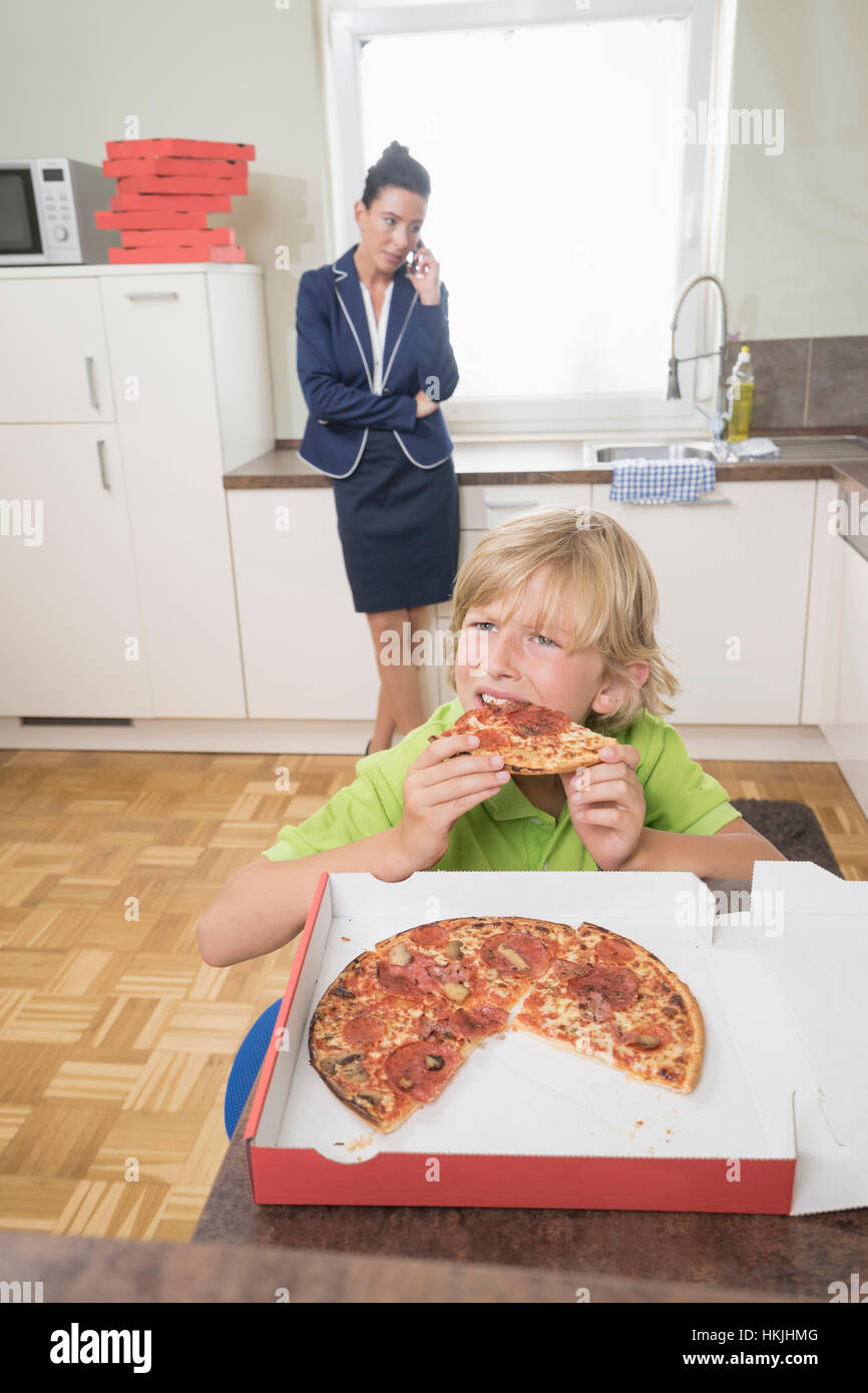 Boy eating pizza alors que la mère est en appel d'affaires,cuisine,Allemagne Bavière Banque D'Images