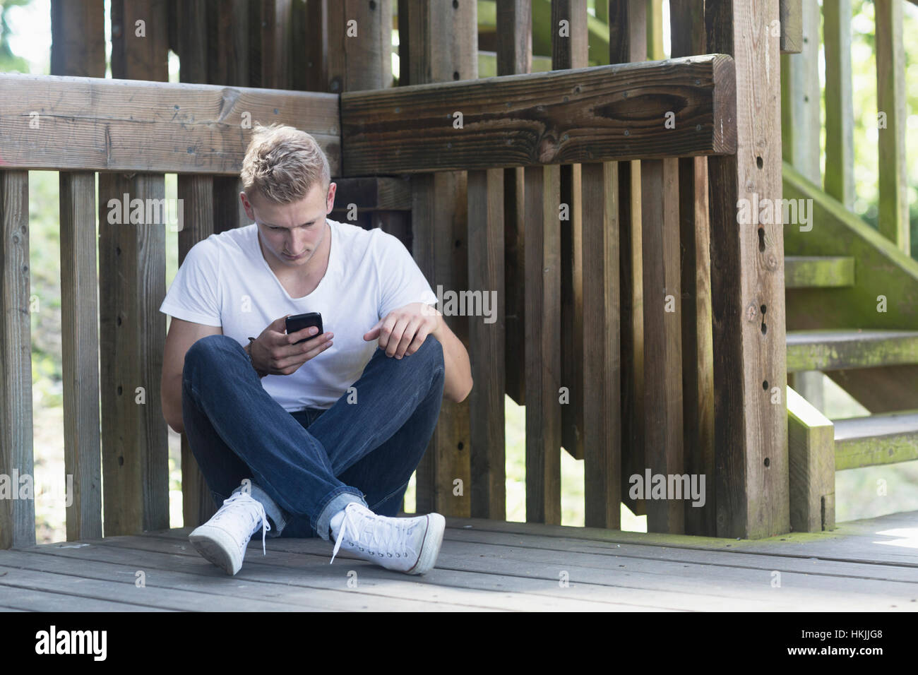 Jeune homme à l'aide de téléphone mobile sur plancher, Freiburg im Breisgau, Bade-Wurtemberg, Allemagne Banque D'Images