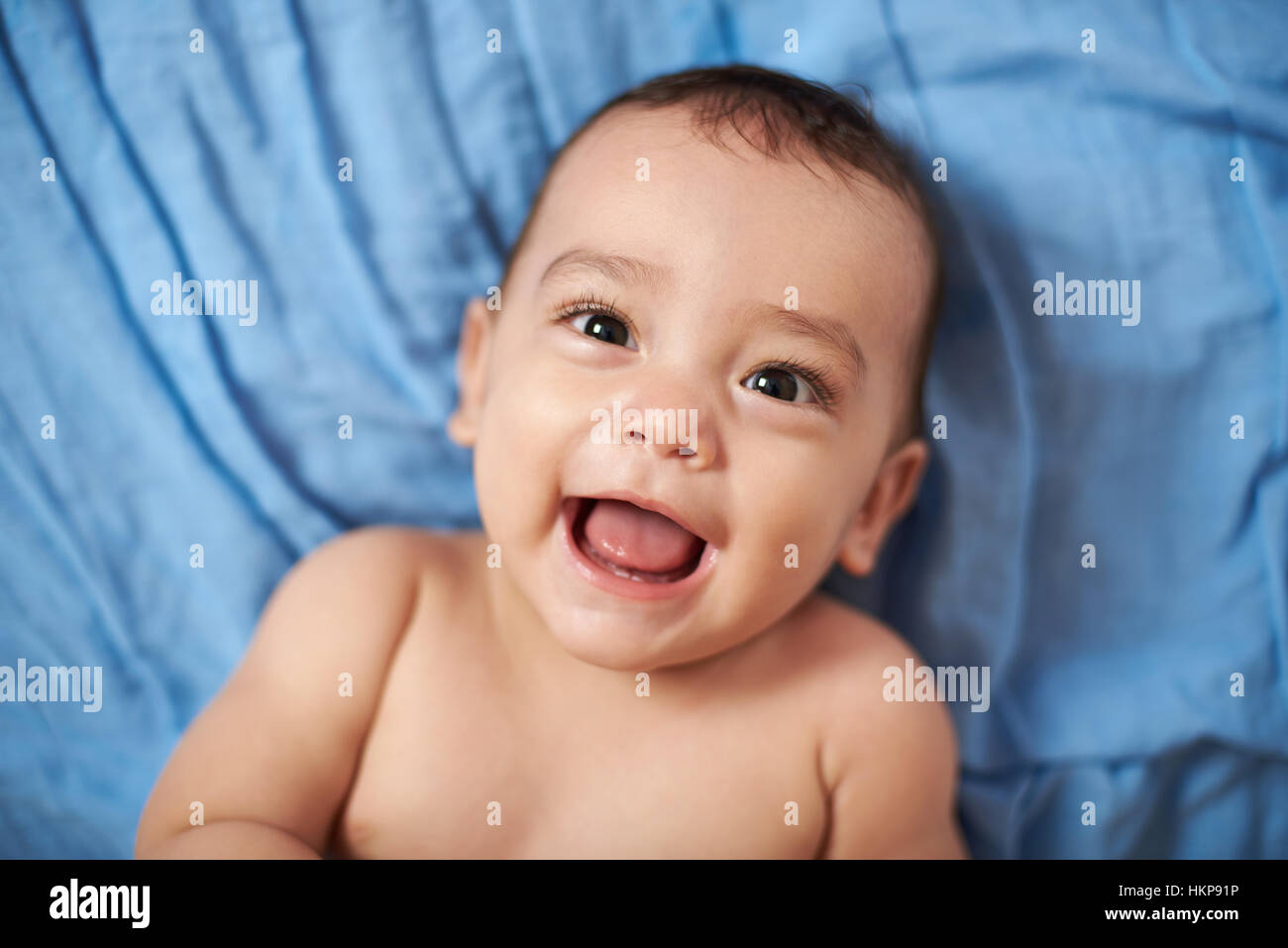 Smiling baby laying on bed couverture bleue close up Banque D'Images