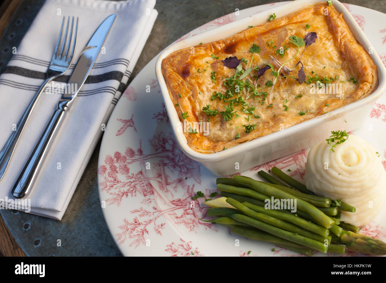 Une tarte feuilletée steak avec garniture, haricots verts, purée de pommes de terre assis sur un coulrful à motifs rose à côté de la plaque d'un couteau et fourchette sur une serviette. Banque D'Images