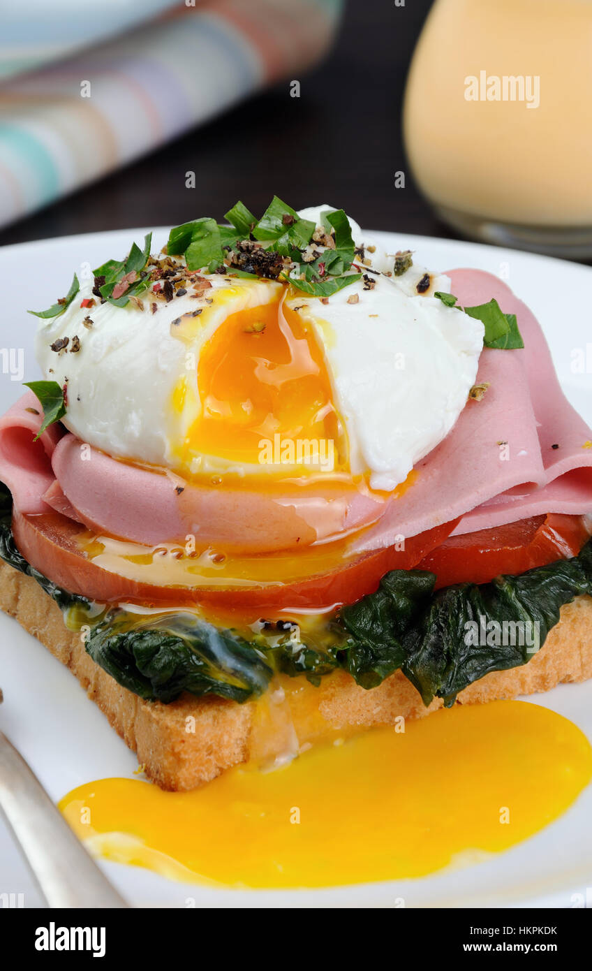 Œufs pochés sur des toasts avec de la tomate, le jambon, les épinards, les épices et fines herbes Banque D'Images