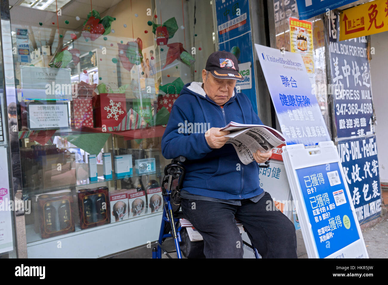Un homme chinois lire un journal tout en étant assis sur une balade dans le quartier chinois, le centre-ville de Flushing, Queens, New York City Banque D'Images