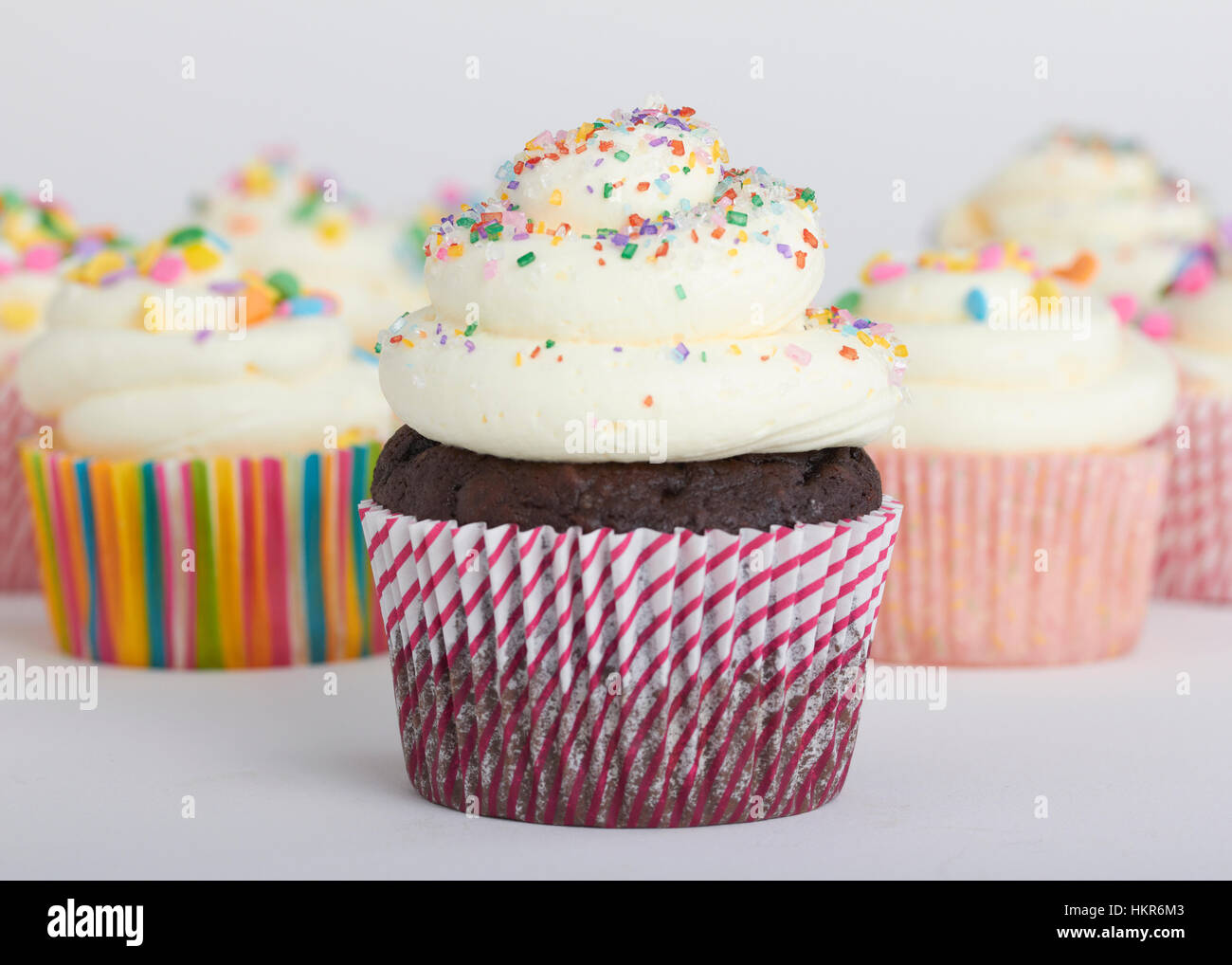 Une douzaine de petits gâteaux au chocolat blanc et à la vanille et glaçage sprinkles multicolores. La cupcake wrappers sont intéressants et mixte imprime/Motif Banque D'Images
