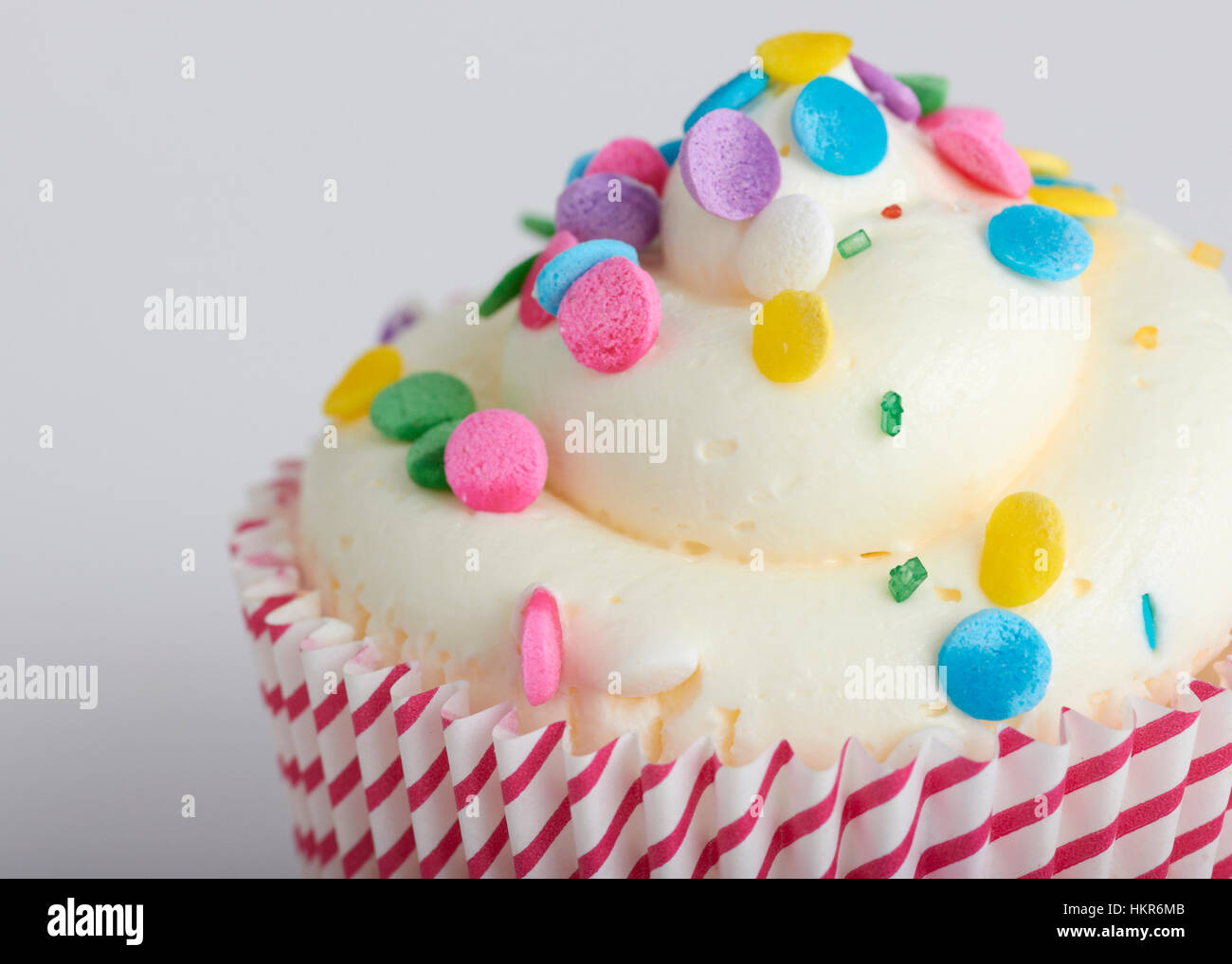 Un close up image d'un petit gâteau avec un tourbillon de glaçage blanc et multi colored sprinkles mixtes sur le dessus. L'un rouge et a cupcake blanc rayé pack Banque D'Images