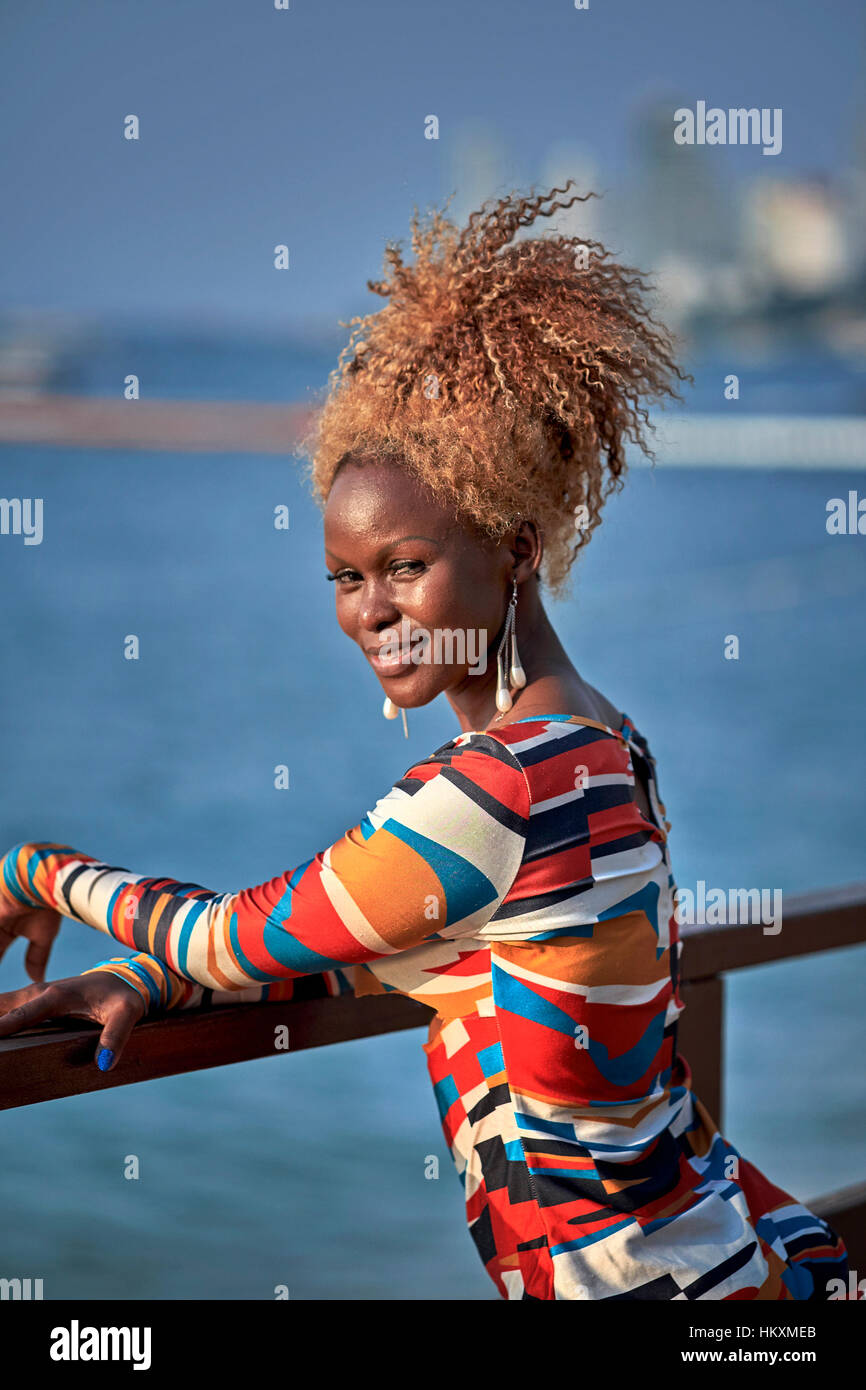 Portrait d'une belle jeune femme africaine avec un attaché crépus coiffure Afro Antillais orange et portant une robe de couleur multi frappante. Banque D'Images