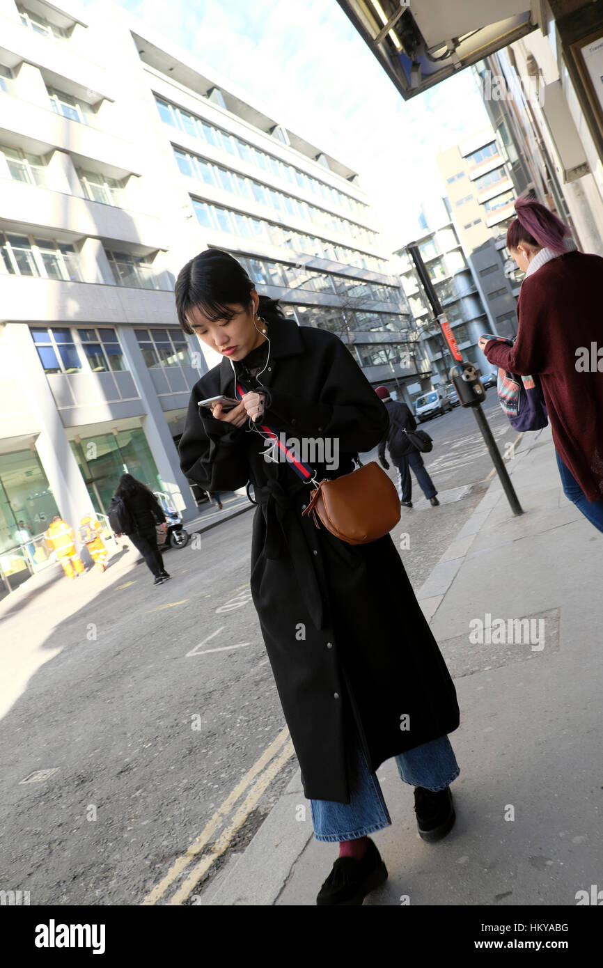 Une jeune femme chinoise balade le long d'une rue de SMS sur téléphone cellulaire mobile mains libres à l'écoute de l'ipod Moorgate dans City of London UK KATHY DEWITT Banque D'Images Une jeune femme chinoise balade le long d'une rue de SMS sur téléphone cellulaire mobile mains libres à l'écoute de l'ipod Moorgate dans City of London UK KATHY DEWITT Banque D'Images