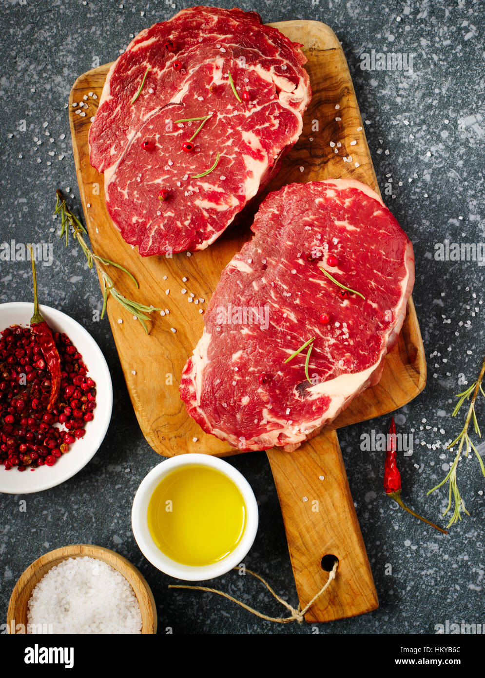 Ribeye Steak cru viande fraîche avec le romarin, le poivre, le sel et l'huile d'olive sur fond ardoise Banque D'Images