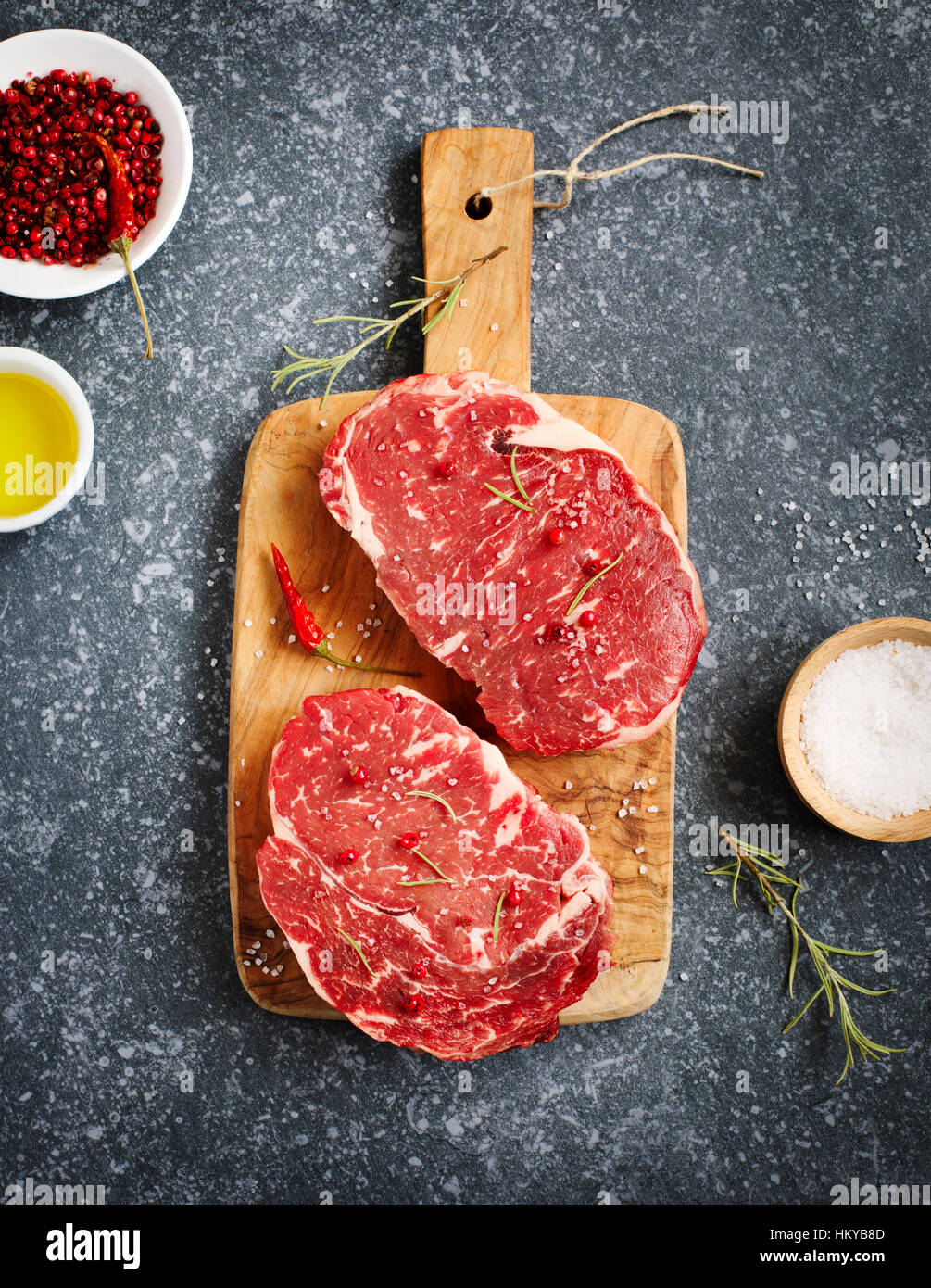 Ribeye Steak cru viande fraîche au romarin, poivre, sel de mer et d'huile d'olive sur fond ardoise Banque D'Images