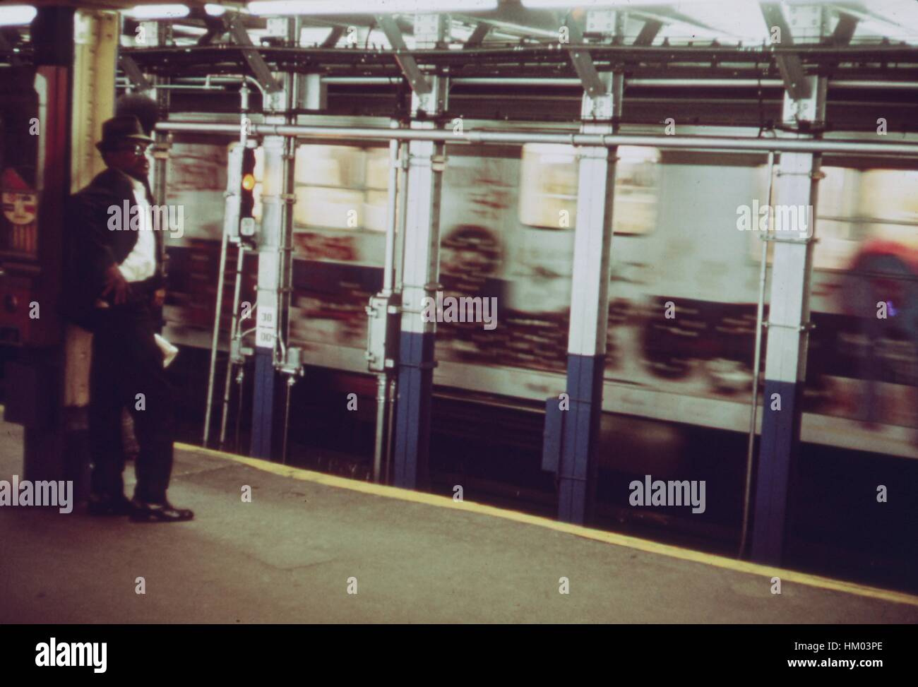 Un homme se tient sur une plate-forme de la station de métro comme un métro train voiture, couverts de graffitis, passe par à New York City, New York, mai 1975. L'image de courtoisie des Archives nationales. Banque D'Images