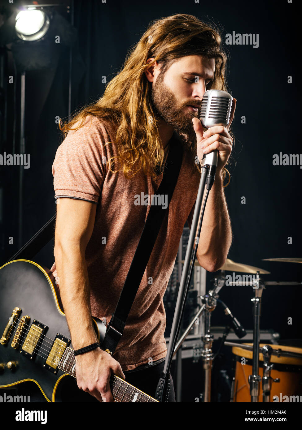 Photo d'un jeune homme aux cheveux longs et la barbe chantant et jouant de la guitare électrique sur scène. Banque D'Images