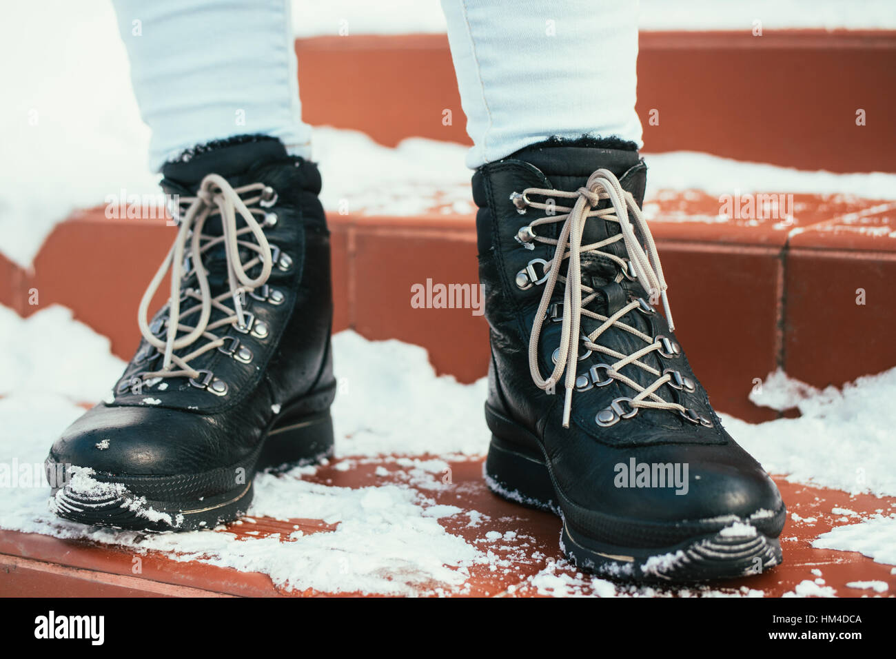 Pieds femelles en hiver des bottes noires avec lacets sont sur l'escalier rouge dans la neige Banque D'Images