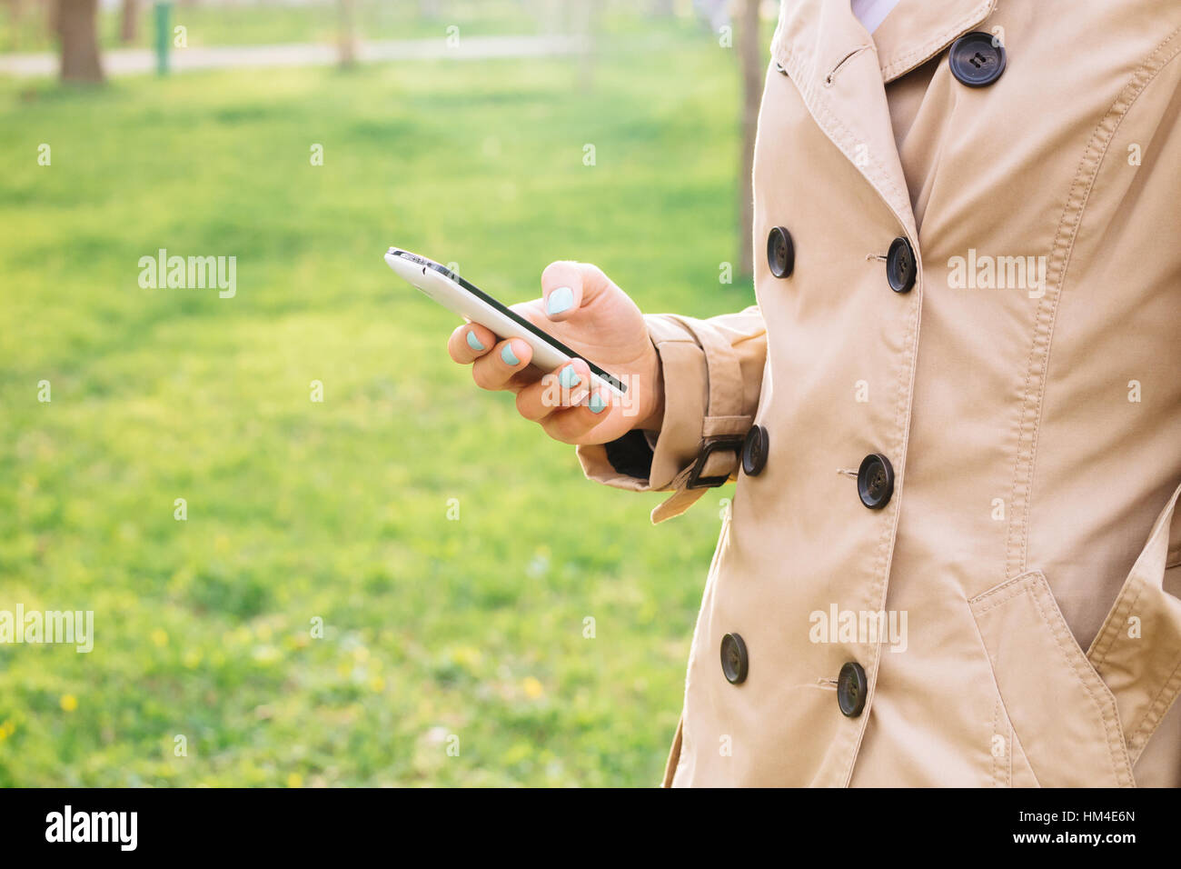 Femme en manteau beige élégante utilise un téléphone cellulaire dans le parc Banque D'Images