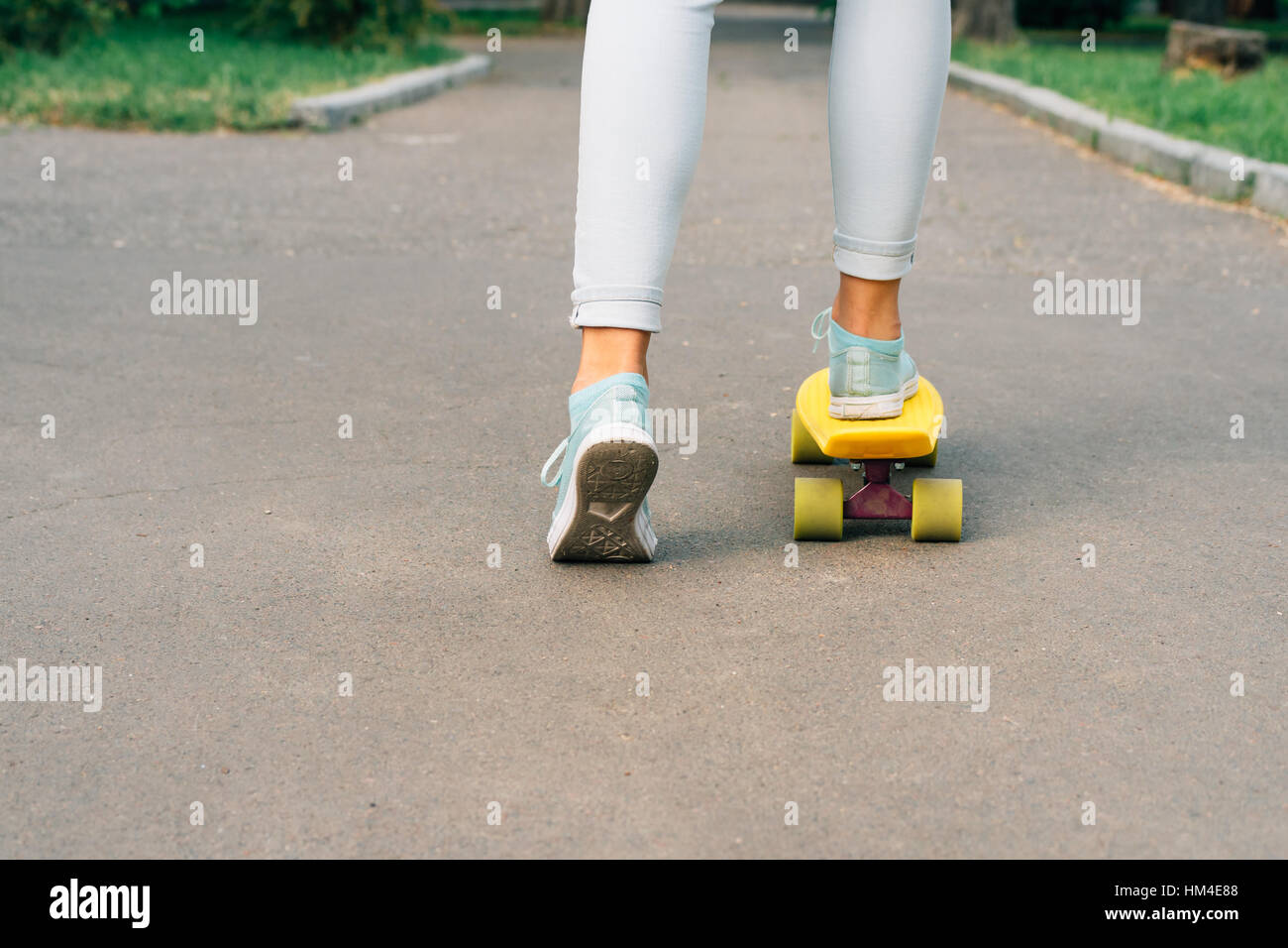 Jeune fille en jeans et baskets équitation une planche à roulettes dans le parc Banque D'Images