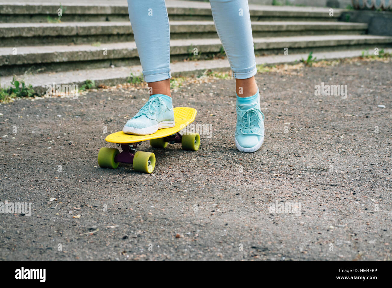 Close-up de femmes jambes en jeans et baskets équitation une planche à roulettes dans le parc Banque D'Images