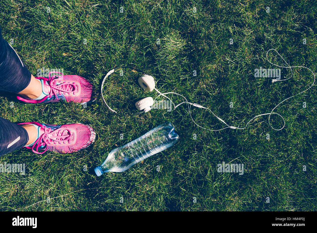 Les jambes des femmes en rose sneakers, casque blanc et une bouteille en plastique d'eau sur l'herbe verte Banque D'Images