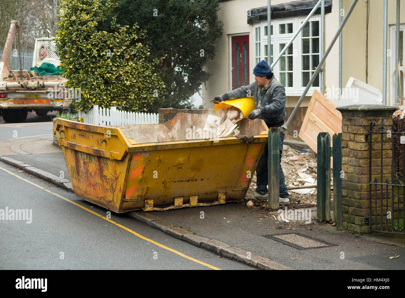 Déchets déchets constructeurs skip, sur la chaussée, la ligne jaune et d'être rempli / chargé builder chargement en camion saute attend. UK Banque D'Images