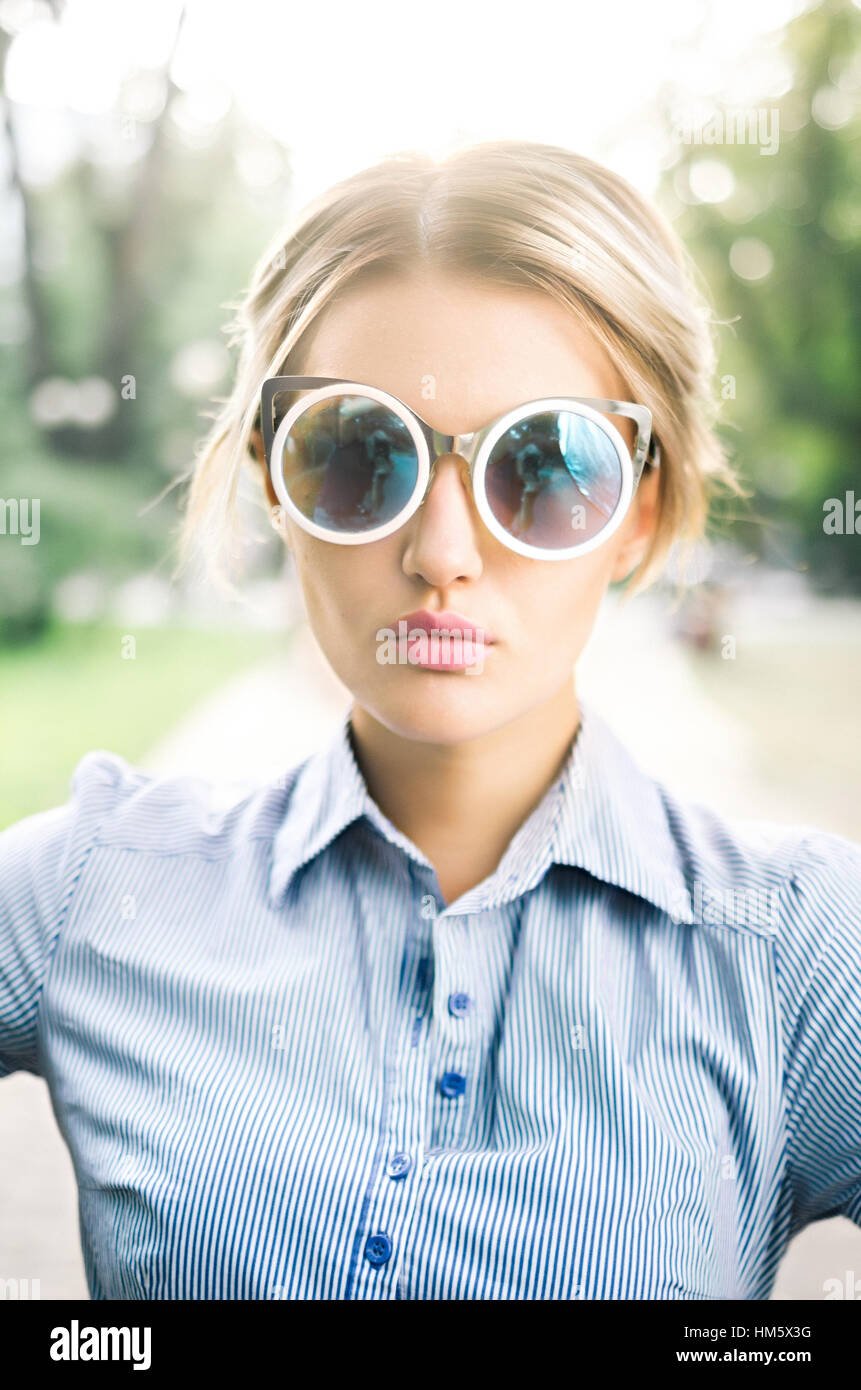 Portrait plein air de belle jeune fille portant des lunettes de soleil réfléchissantes et robe casul illuminée par l'éclairage solide Banque D'Images