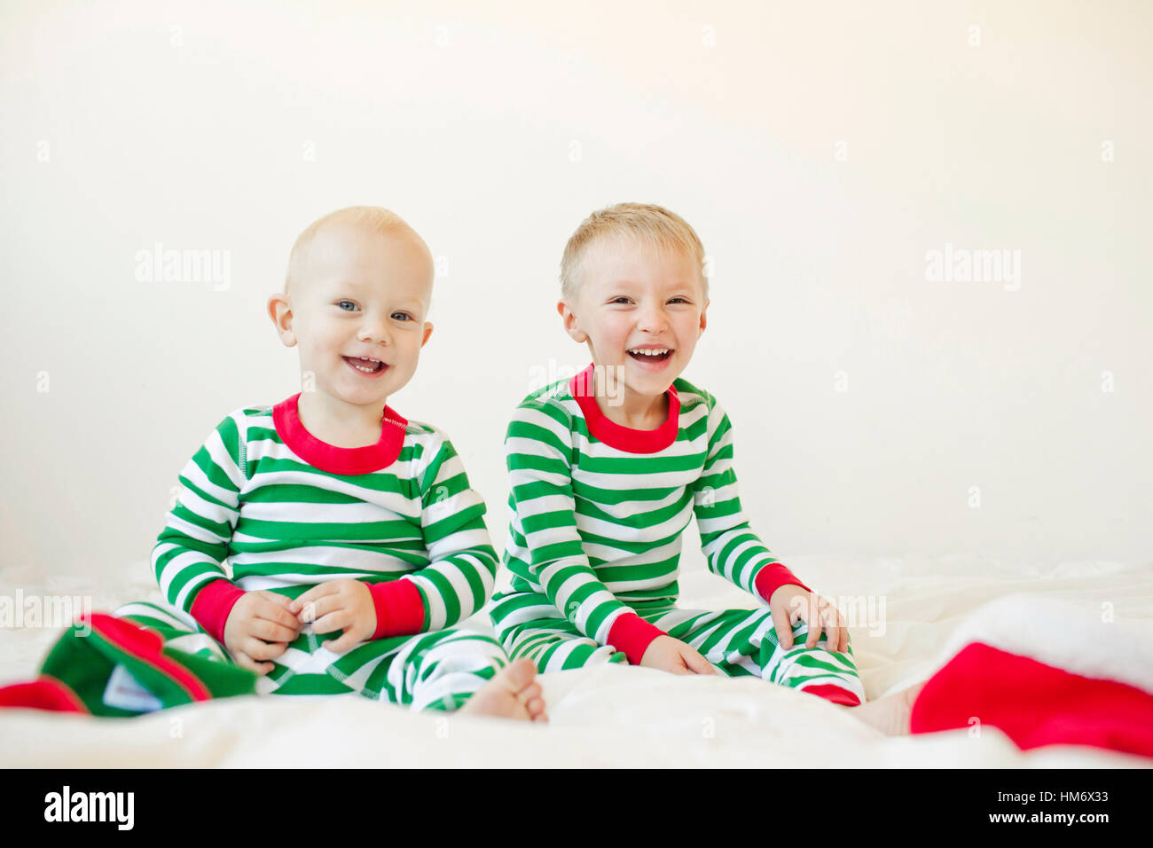 Portrait of smiling baby boys sitting on bed against white background Banque D'Images