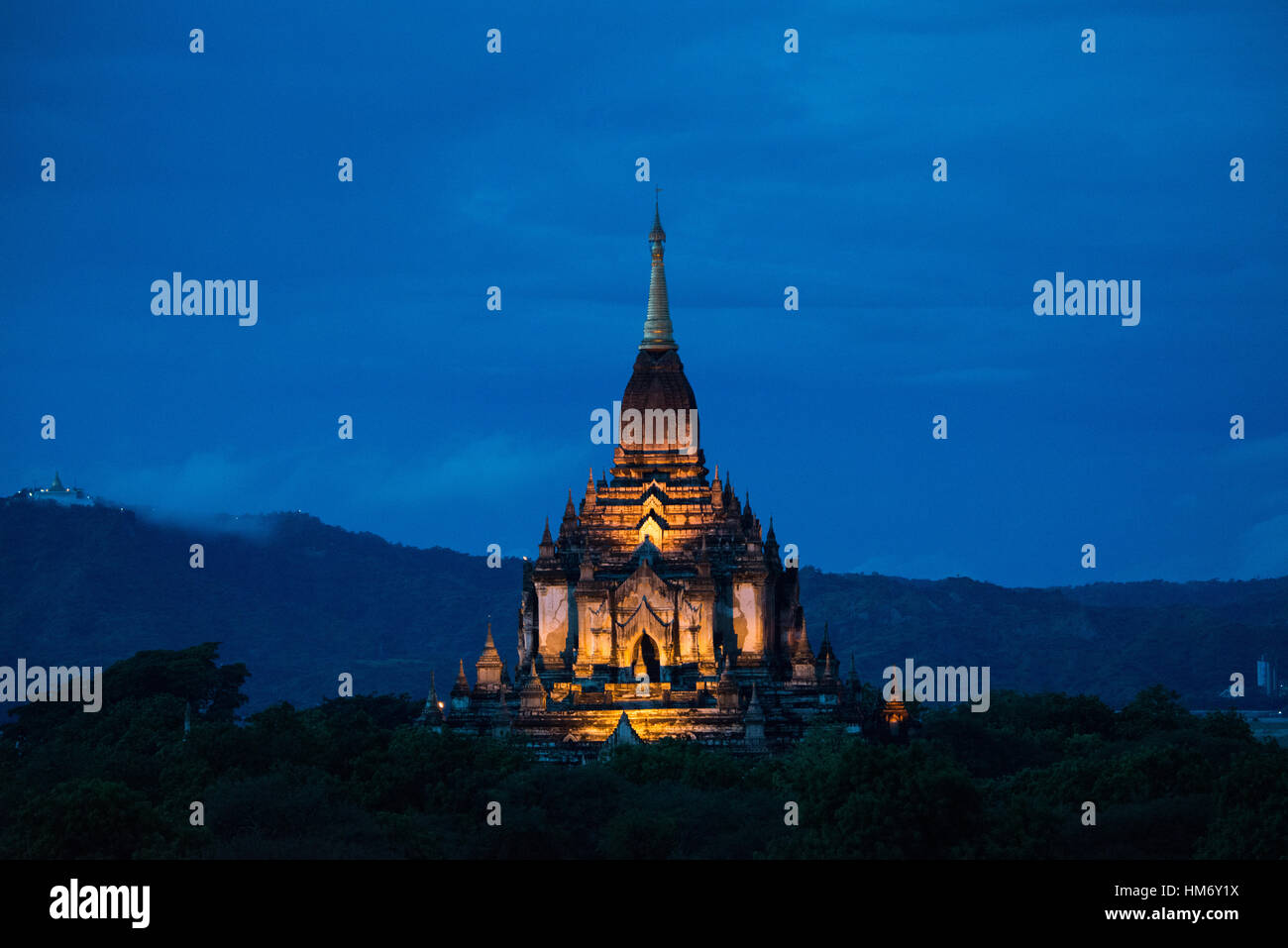 Temple bouddhiste au crépuscule Bagan Myanmar | BAGAN, Myanmar — Une flèche de temple dorée brille contre le bleu profond du crépuscule sur la plaine de Bagan, sa tour sikhara incurvée captant la dernière lumière artificielle avant la nuit. Des milliers de temples en briques et de stupas du Royaume de Pagan, qui a prospéré du XIe au XIIIe siècle, se dressent encore dans cette zone archéologique du patrimoine mondial de l'UNESCO sur la rivière Ayeyarwady. Banque D'Images
