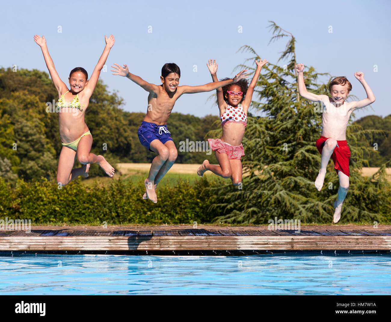 Groupe d'enfants de sauter dans une piscine extérieure Banque D'Images