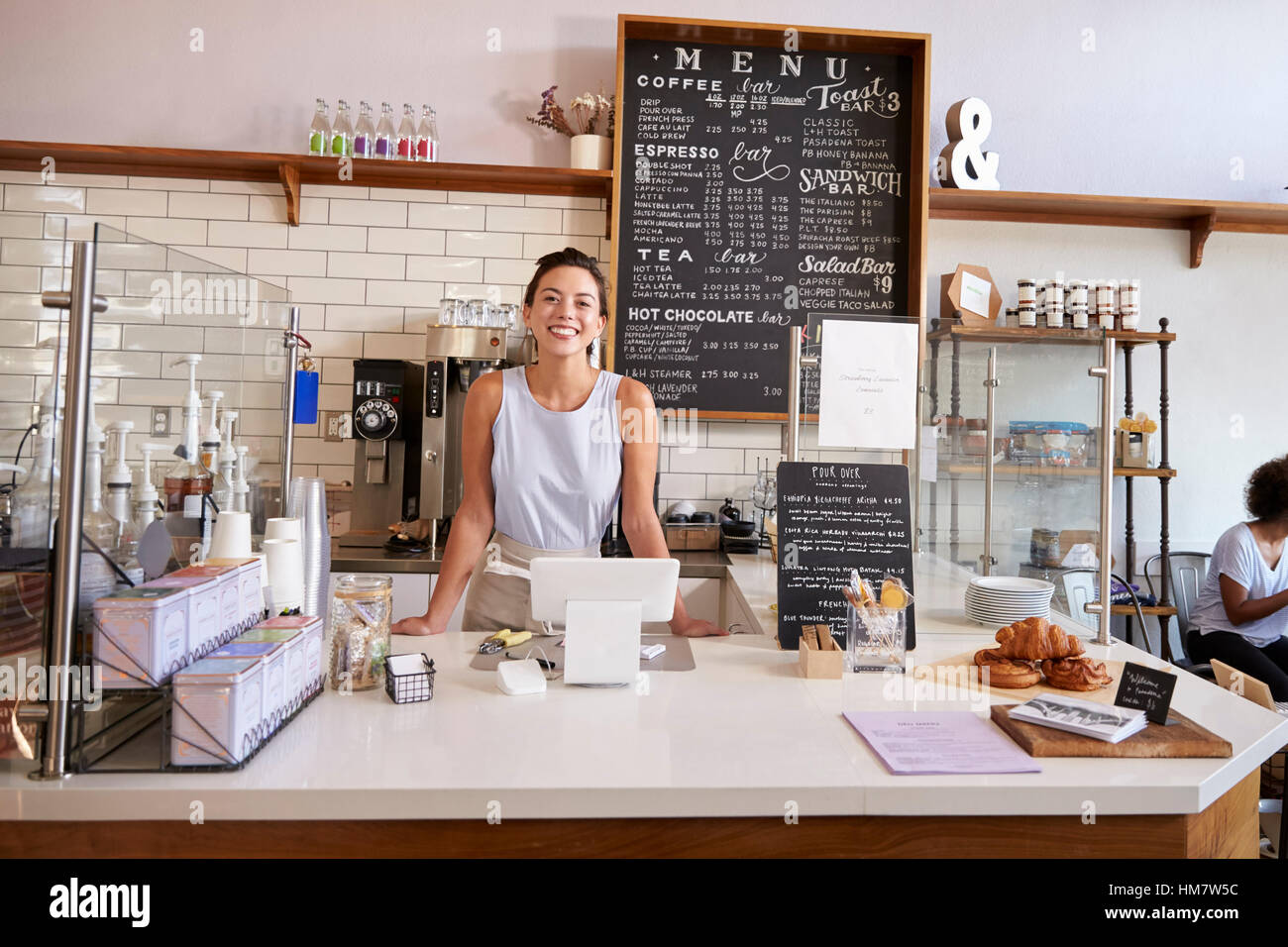 Femme derrière le comptoir d'un café à la recherche à l'appareil photo Banque D'Images