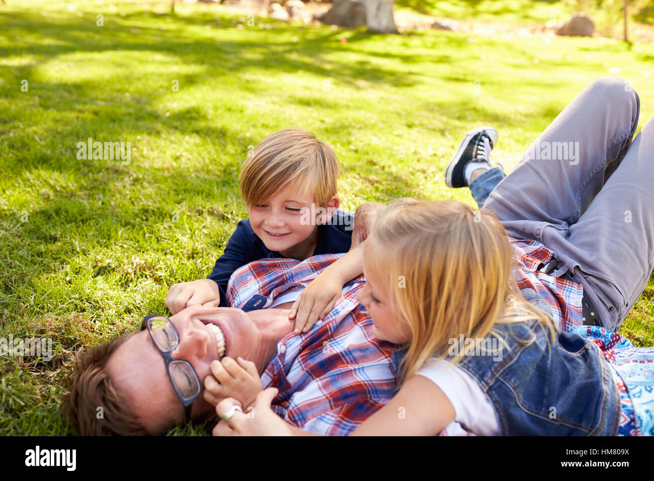 Deux enfants qui jouent avec leur père, couché dans un parc, vue latérale Banque D'Images
