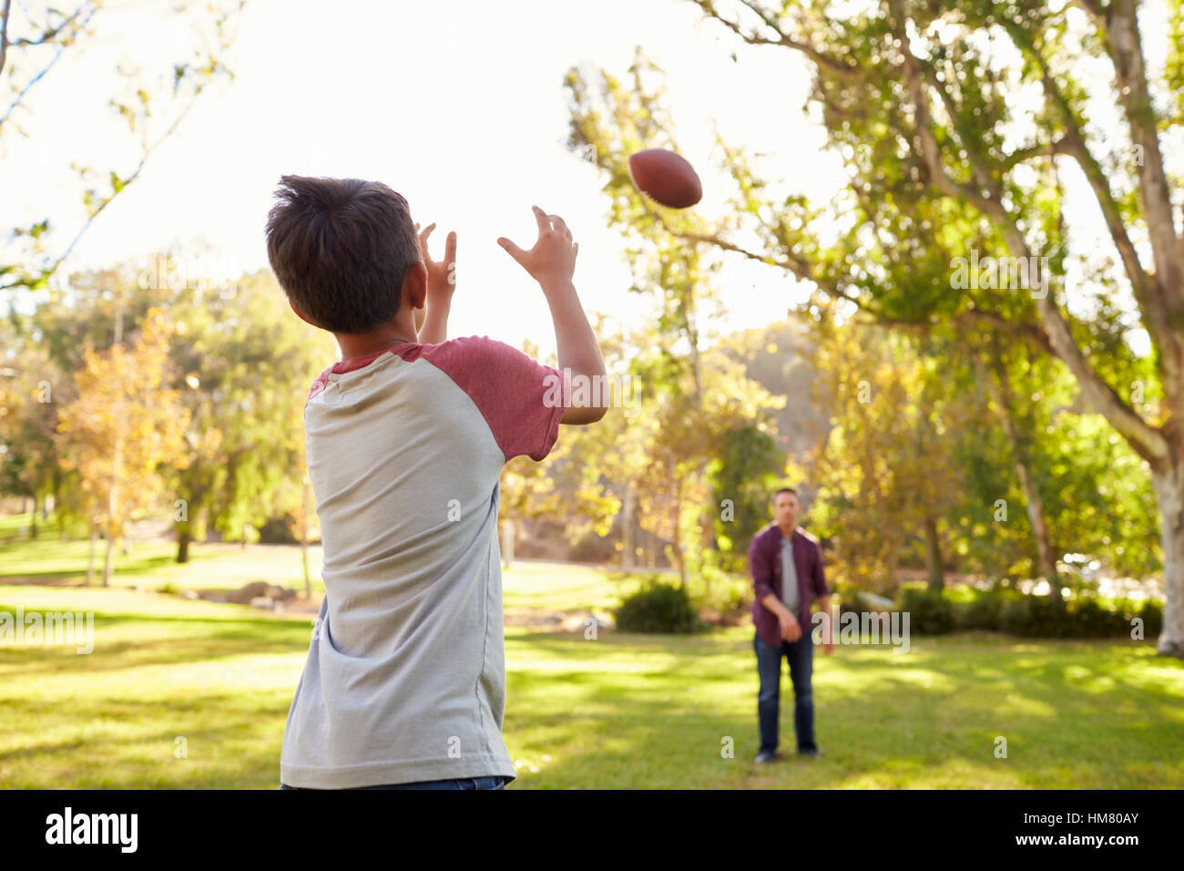 Père et fils de jeter le football américain à l'autre dans le parc Banque D'Images