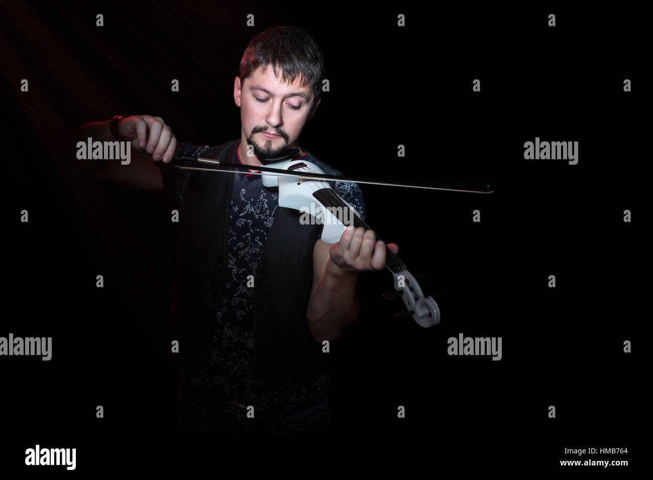 Jeune violoniste barbu jouant sur violon électrique blanc sur un fond noir Banque D'Images