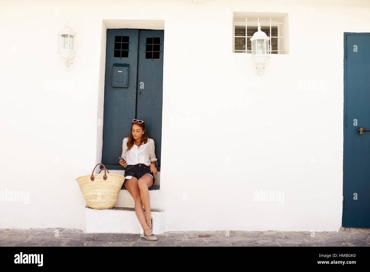 Jeune femme en vacances assis sur les marches à la recherche à son téléphone Banque D'Images