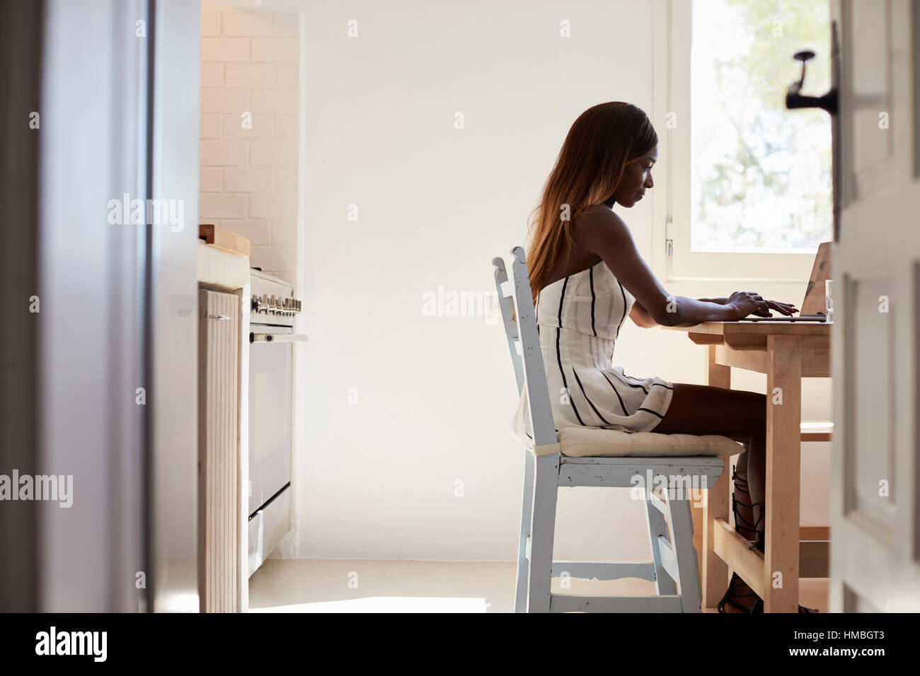 Jeune femme assise dans sa cuisine à l'aide d'un ordinateur portable Banque D'Images