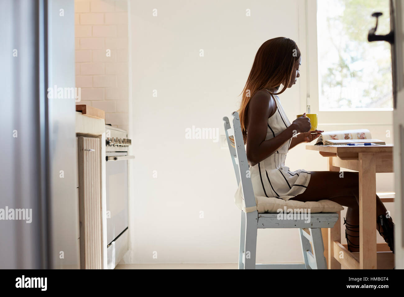 Jeune femme assise dans la cuisine à boire du café et de la lecture Banque D'Images