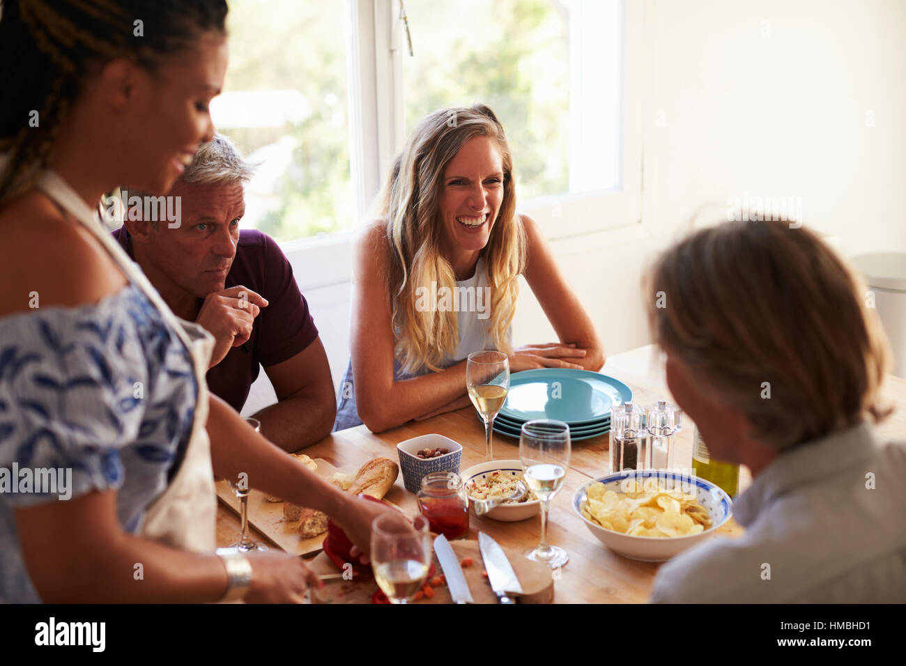 Amis parler à table de cuisine tout en femme prépare la nourriture Banque D'Images