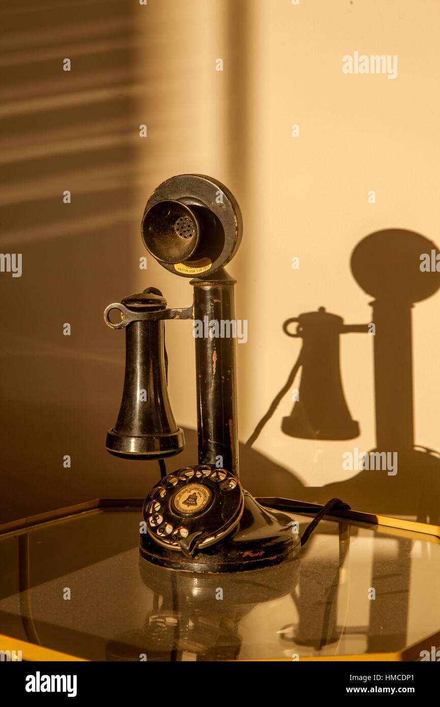 Un chandelier noir téléphone à cadran rotatif est assis sur une table en verre avec des ombres sur le mur. Banque D'Images