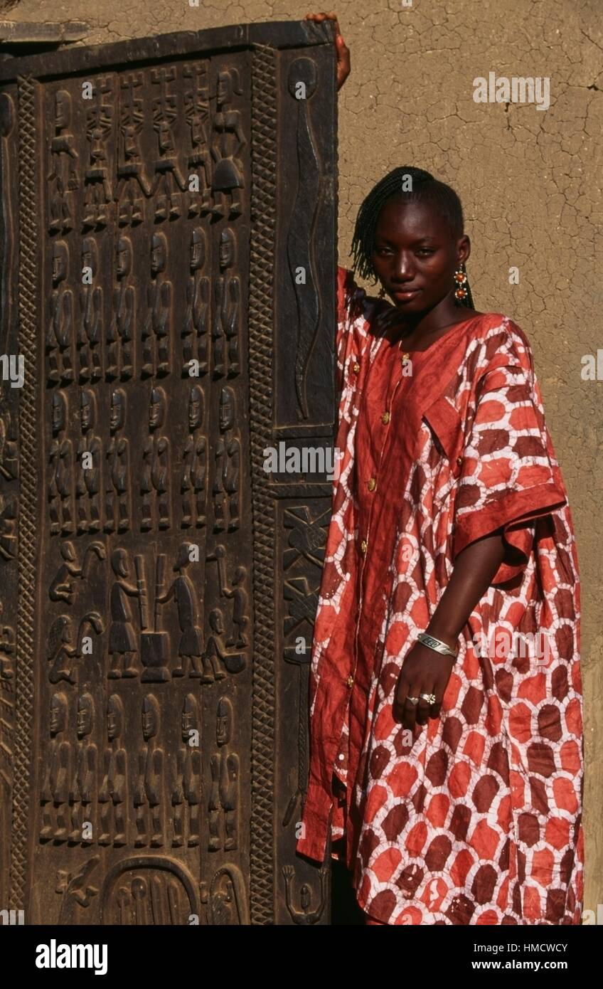 Une jeune femme Dogon à côté d'une porte sculptée, village Sangha, Bandiagara, Mali. Banque D'Images