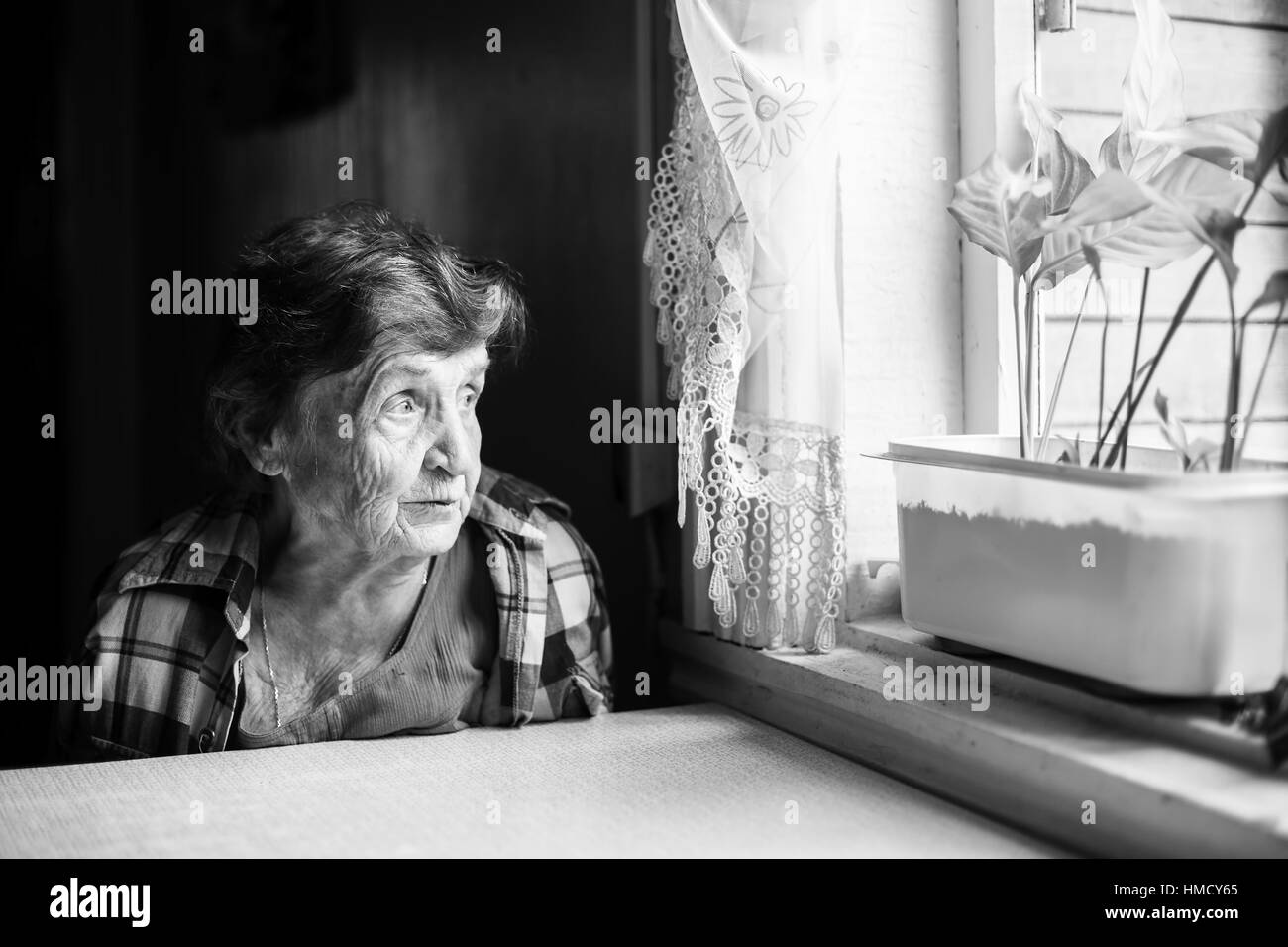 Une femme âgée malheureusement en regardant par la fenêtre. Le noir et blanc. Banque D'Images